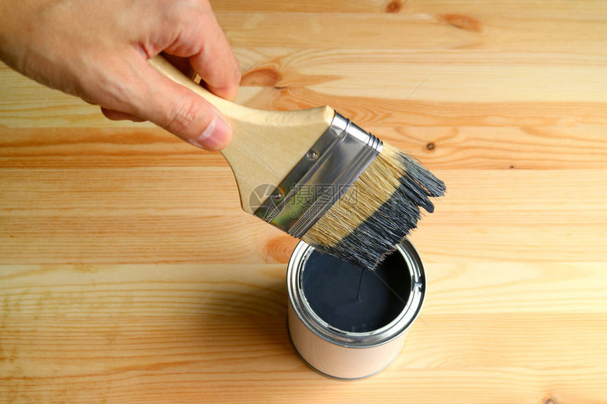手持油漆刷子涂在木板上的油漆罐中图片