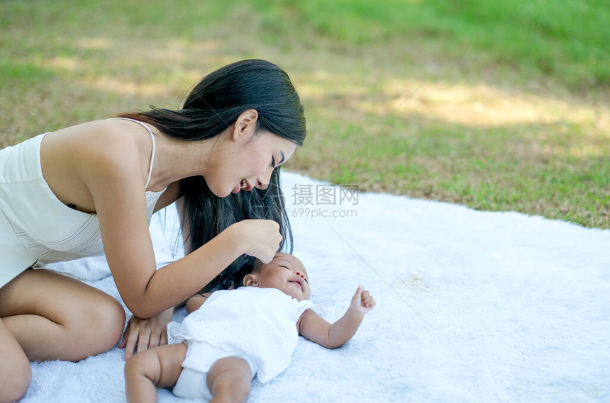 年轻的亚洲美丽的母亲在花园的白地毯上和她的小宝玩图片