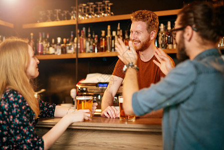 坐在酒吧柜台喝啤酒和跟酒保聊天的好朋友图片