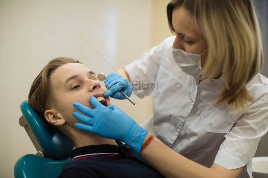 女牙医在诊所的牙科椅上对男孩进行牙齿检查图片
