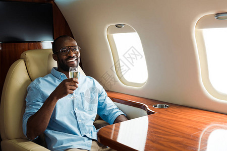 戴着眼镜的非洲男子在私人飞机上举着香槟杯图片