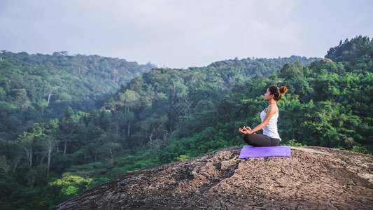 亚洲妇女在假期放松玩瑜伽山岩崖上泰国山林的质年轻女子在自然女幸福中练习瑜背景图片