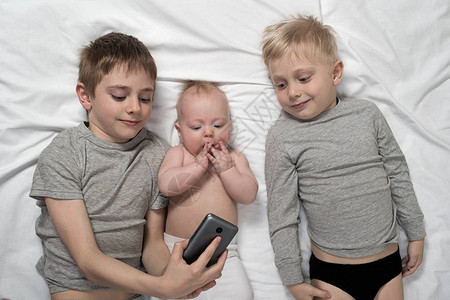 两个兄弟带着一个最小的孩子躺在白床上图片