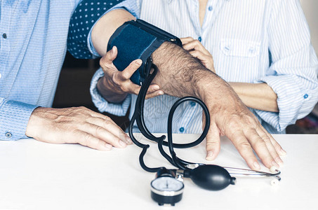治疗师的女用手与典型的测量男子在白桌子上家中血压图片