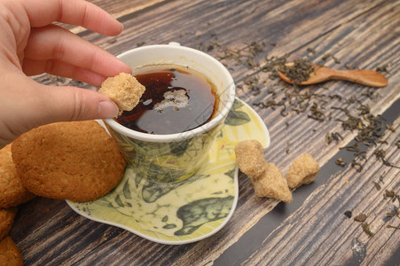 女孩的手把一块棕色糖放进一杯黑茶燕麦饼干茶叶图片