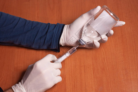男医生用橡胶手套握着注射器和木制桌上的液态药物瓶子图片