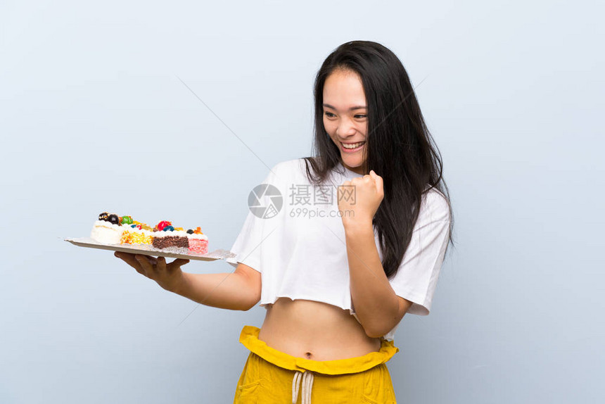 年轻时的少女拿着许多不同的小蛋糕庆祝一场胜图片
