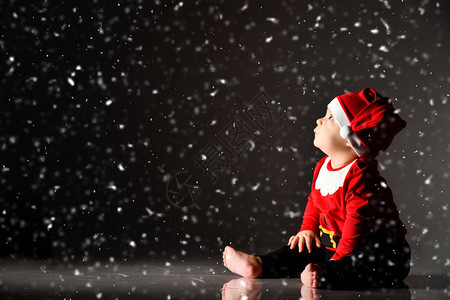 戴着红色圣诞帽和新年服装的微笑男婴正坐在雪下的冰上图片