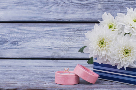 订婚戒指在盒子和木制背景上的白色菊花图片
