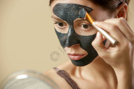 美丽的女人在脸上涂净化的黑面罩图片