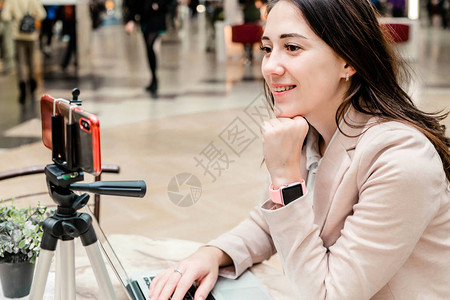 一位年轻女博主在购物中心的照片在笔记本电脑前工作进行直播录制视频与她的社交网络背景图片