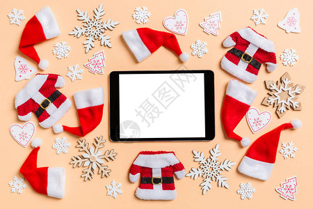 带有圣诞装饰品和橙色背景的圣诞老人帽子的数字平板电脑最佳视图图片
