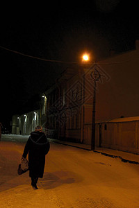 妇女沿着一个夜晚的冬季小巷行走被图片