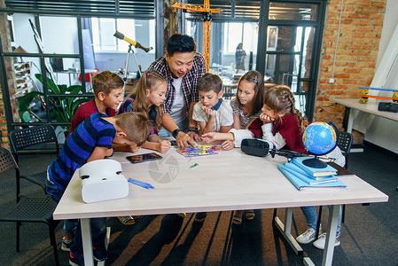 六名聪明的学童与亚洲男教师一起研究带风扇和灯泡的电子构造器有创造力的学生与科学家在学校背景图片