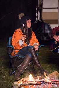 坐在营地火场附近的烤棉花糖的年轻女士图片