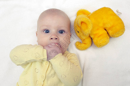 小男孩的笑脸几个月前咬他的拳手躺在床上与柔软的玩具黄大象图片