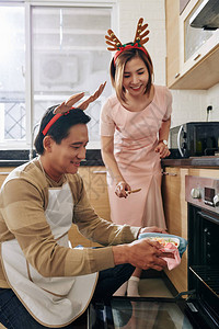 微笑的漂亮亚洲女人看着她的丈夫把锅盘和圣诞餐图片