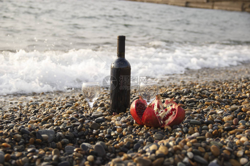 成熟的石榴果与一杯酒和一瓶在海滩上在海边浪漫的一天背景是海浪和大海婚礼或情人节庆图片