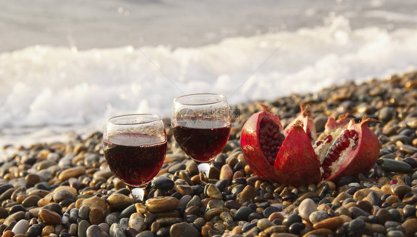 成熟的石榴果配上海滩上的一杯酒在海边浪漫的一天背景是海浪和大海婚礼或情人节庆图片