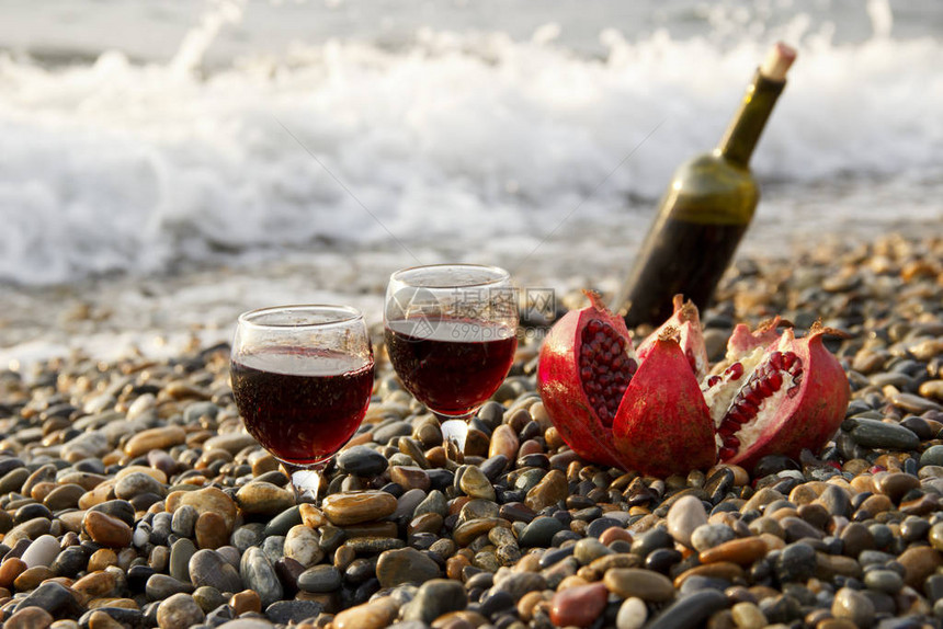 成熟的石榴果与一杯酒和一瓶在海滩上在海边浪漫的一天背景是海浪和大海婚礼或情人节庆图片