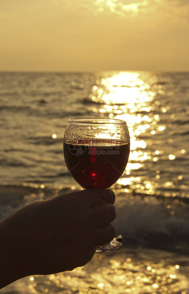 他手上的红酒杯日落时在海边浪漫的日子婚礼或情人节的庆祝活动的概图片