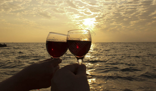 两杯红酒手握着日落时海边浪漫的一天婚礼或情人节庆祝活动的概念图片