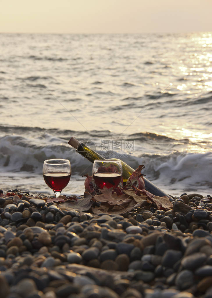 成熟的石榴果与一杯酒和一瓶在海滩上在海边浪漫的一天背景是海浪和大海岸边躺着泛黄的树叶婚礼或情人节庆图片