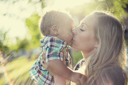 美丽快乐的母亲在夕阳的光下抱着她可爱的男婴当妈向儿子表达爱意时图片