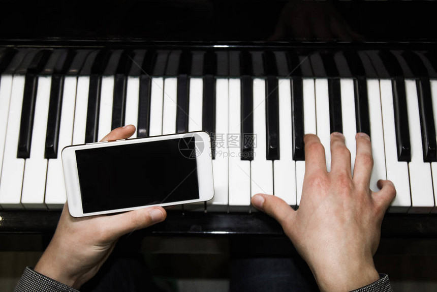 两只男手用智能手机在钢琴上图片