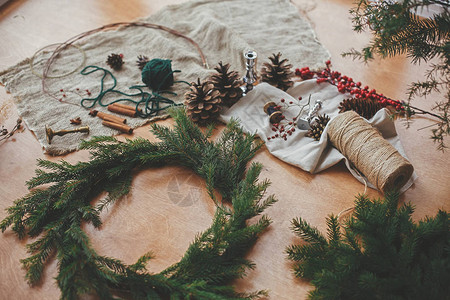 制作圣诞花环木桌上的冷杉树枝松果线浆果肉桂质朴的圣诞花环工作坊图片