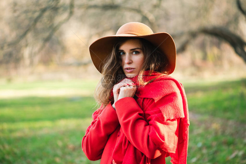 美丽的黑发年轻女子在秋季公园背景下穿着大衣和围巾的全红色外观身穿红色外套和棕色帽子的女孩双手靠近图片