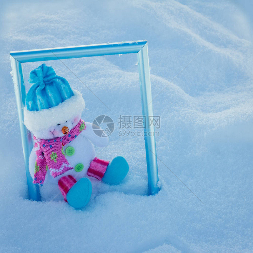 圣诞玩具雪人戴着蓝色帽子坐在雪堆里图片