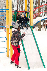 母亲帮助她的小儿子滑下梯一家人在寒冷的冬日一起享受冬装寒假快乐图片