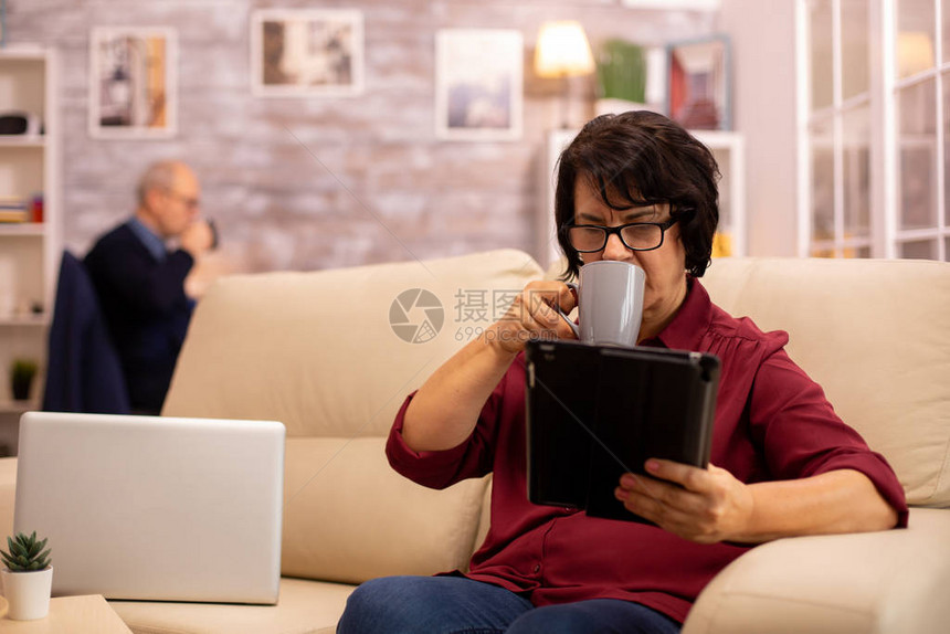 老年妇女坐在沙发上在舒适的客厅里使用图片