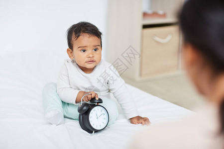 小孩坐在床上玩闹钟妈看着他图片