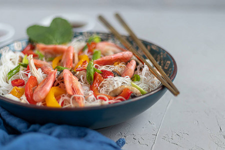 东方米粉乌冬面配甜椒蘑菇和虾海鲜在浅色背景上筷子附近撒了芝麻的图片