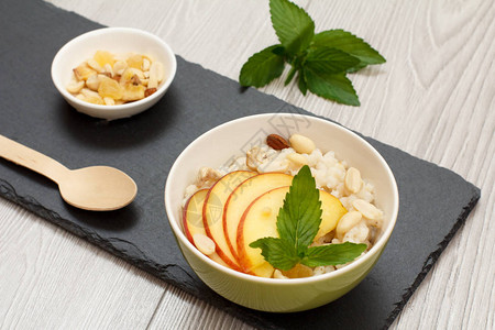 瓷碗配高粱粥配鲜桃腰果和杏仁木勺和石板上的坚果碗纯素无麸质高粱沙图片