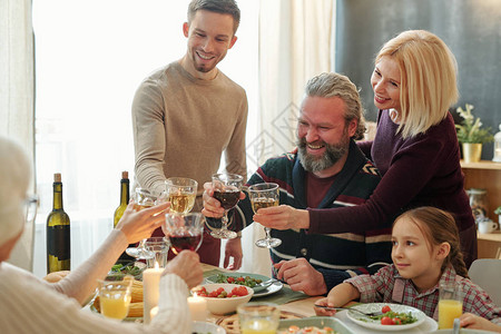 快乐的成熟和年轻家庭成员在晚宴期间用红酒举杯图片