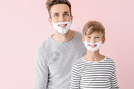 父亲和他的小儿子在颜色背景下脸上涂着剃图片