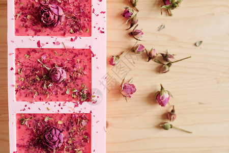上面和附近的小玫瑰花状瓣喷洒的手制粉红色肥皂中填满了硅胶模子的图片