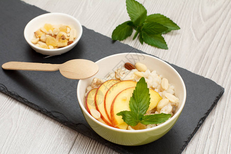 瓷碗配高粱粥配鲜桃腰果和杏仁木勺和石板上的坚果碗纯素无麸质高粱沙背景图片