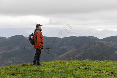 一个登山的成熟男子在路上停下来观察地平线上周围的峰值背景图片