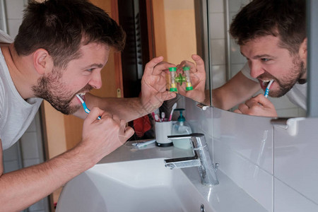 年轻人带着牙刷打扫牙齿看着在家中的卫生间里照镜子在特殊的钟图片