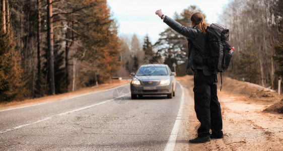 一个年轻人正在全国各地搭便车该男子正试图赶上一辆过往的汽车背着包的人搭背景图片