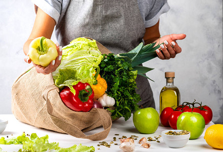 女手中的绿胡椒和在厨房桌上装满新鲜蔬菜的生态友好布袋图片