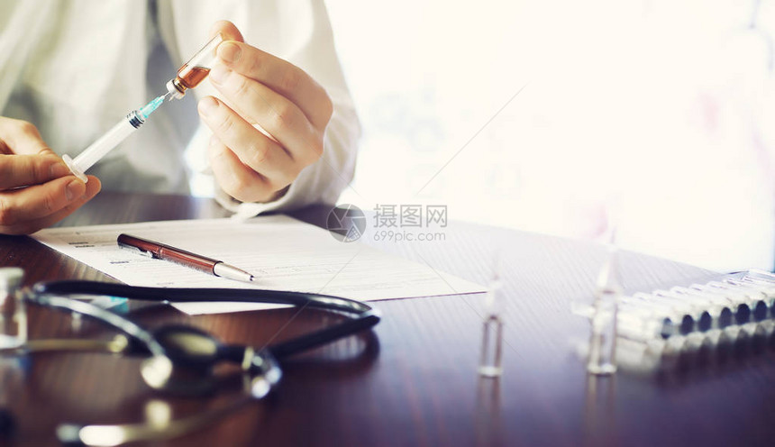 一名男子签署一份医疗文件桌子上的医疗设备听诊器和带注射器的安瓿在办公室做笔图片