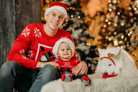 父亲和戴着圣诞老人帽子的小儿子坐在白色萨摩耶犬旁边图片