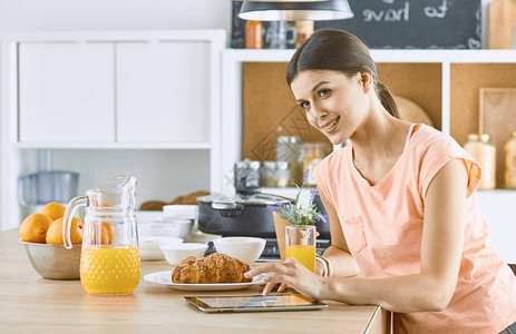 微笑的漂亮女人看着手机拿着橙汁杯子在厨房吃早餐时笑一呢图片
