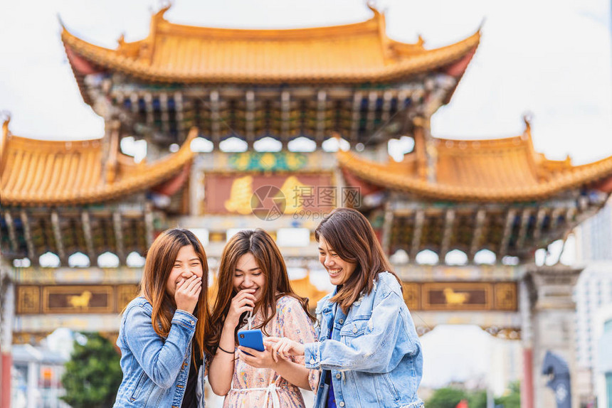 肖像三位亚洲幸福女在昆明金碧广场旅行时笑着使用智能手机进行社交网络图片