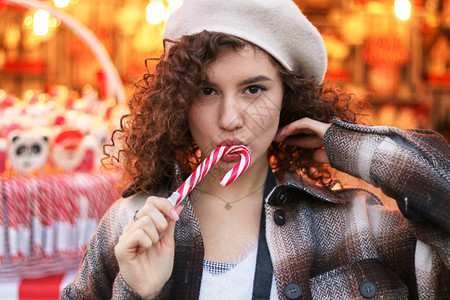 可爱的卷发女孩在圣诞集市上拿着棒糖和微图片